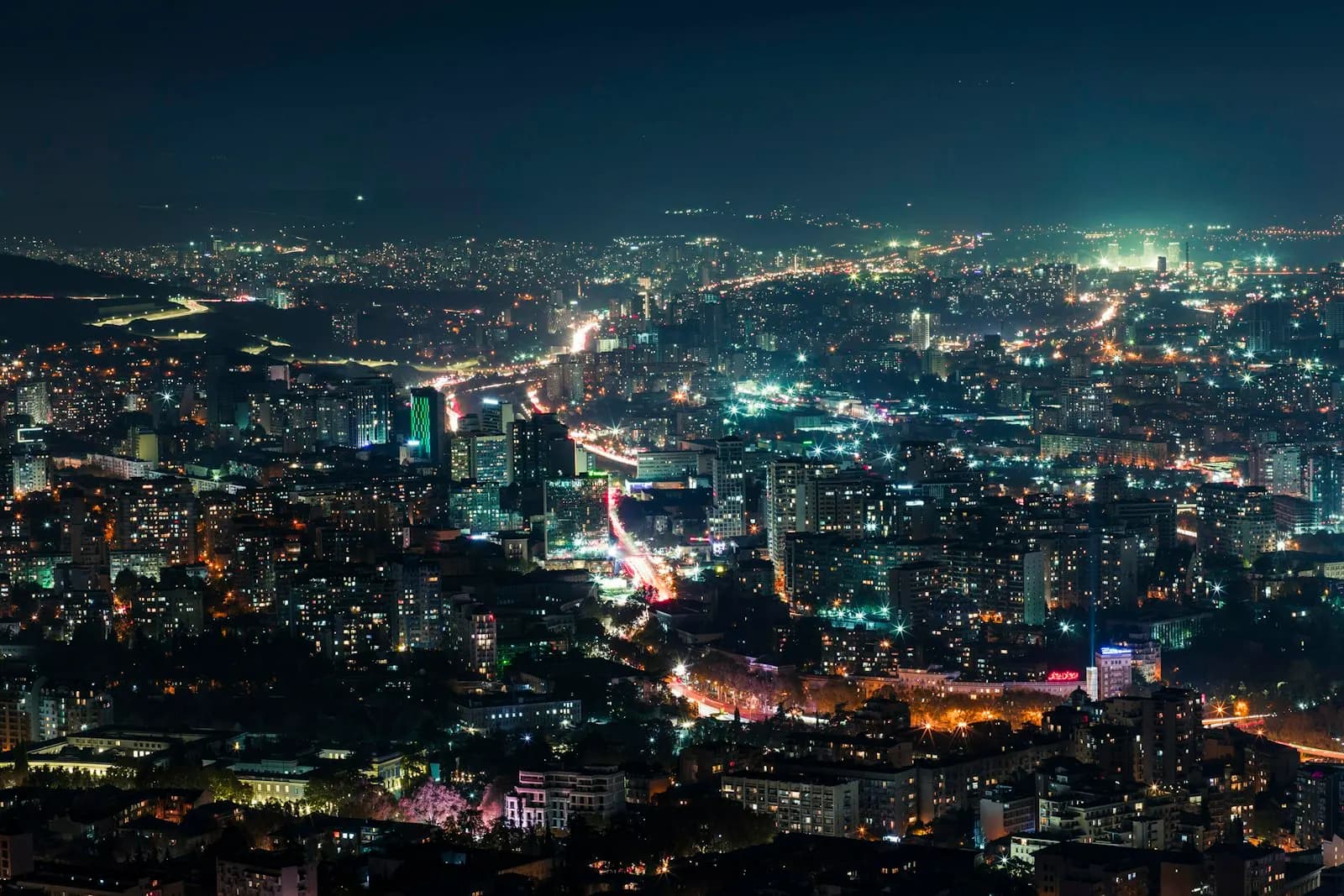 Tbilisi at night seen from a hill, with the lights of the city stretching into the distance.